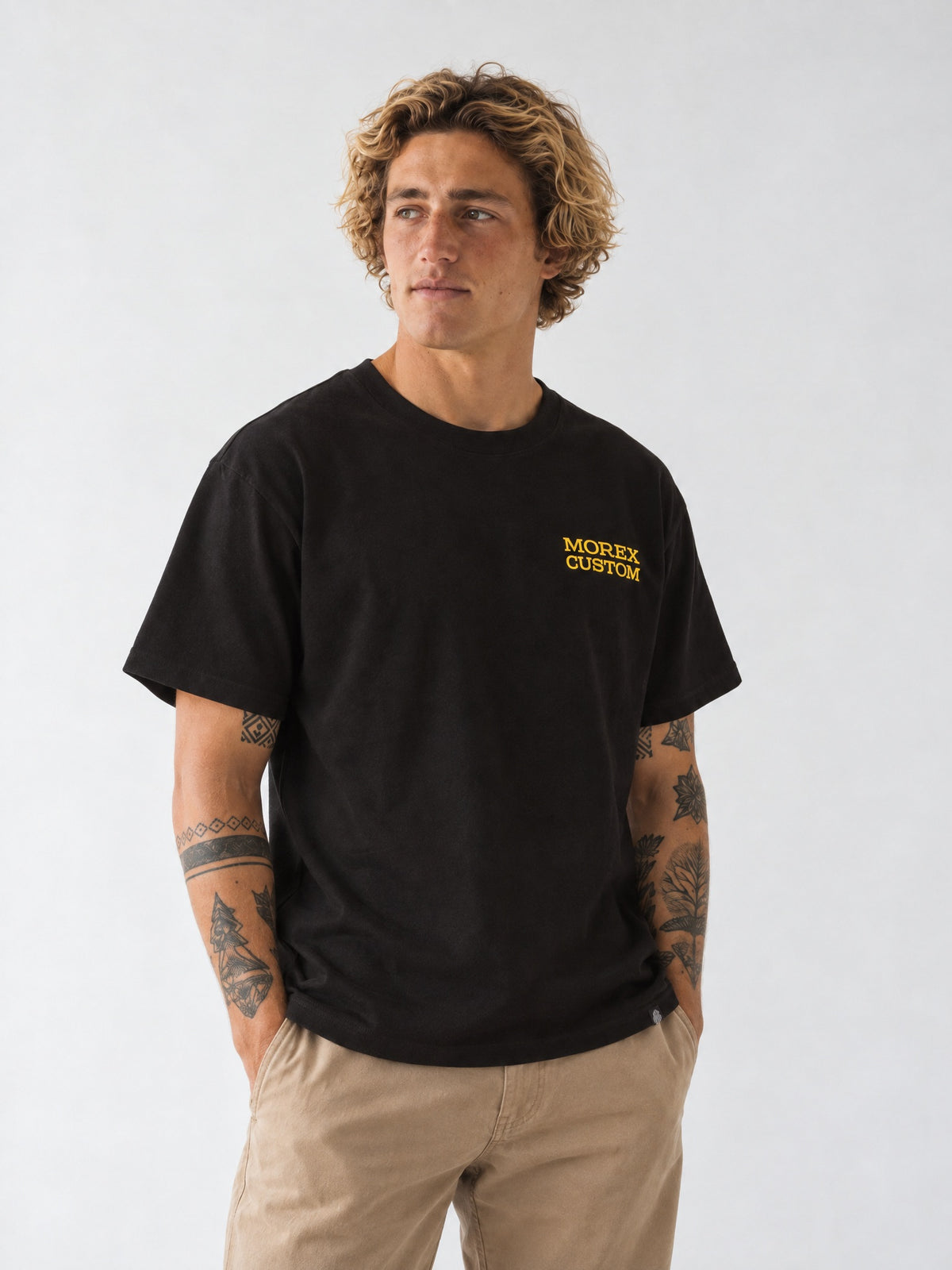 Un homme aux cheveux bouclés portant un t-shirt noir avec le logo Morex Custom brodé en jaune sur la poitrine.