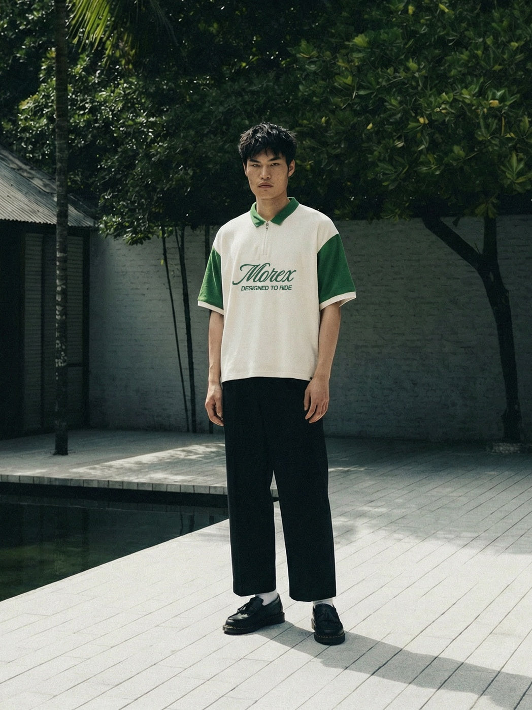 Homme portant un polo Morex Custom bicolore blanc et vert avec un pantalon noir dans un cadre tropical extérieur.