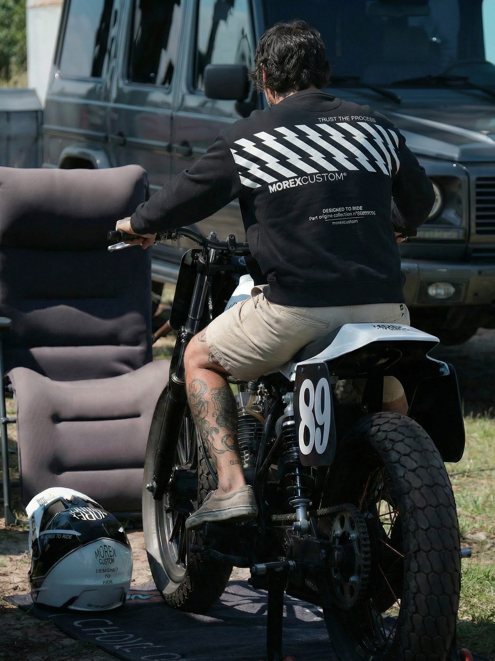 Un homme de dos assis sur une moto de compétition, portant un sweat-shirt Morex Custom noir avec des rayures blanches.