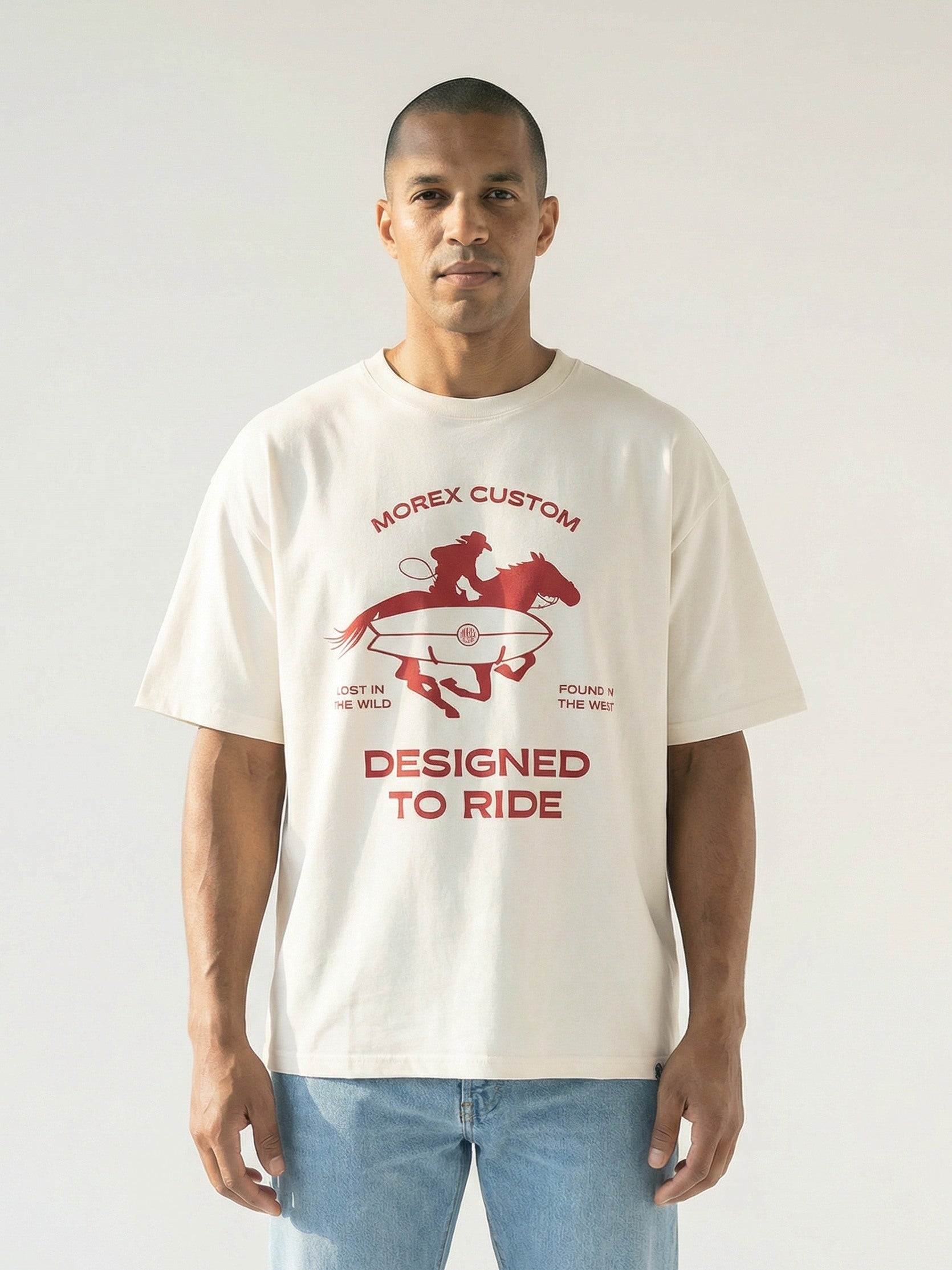 Homme portant un t-shirt Morex Custom blanc cassé avec un graphisme rouge représentant un cavalier et une planche de surf, avec l'inscription Designed to Ride.