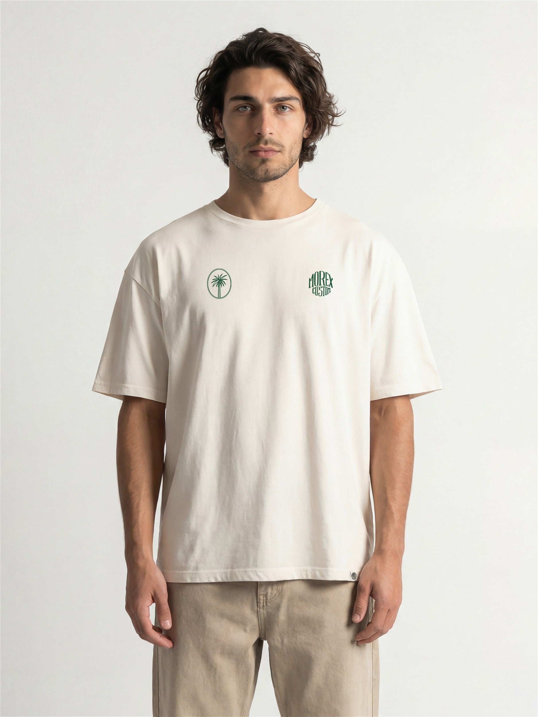 Homme portant un t-shirt blanc cassé de la marque Morex Custom avec deux logos verts sur la poitrine, style lifestyle et décontracté.