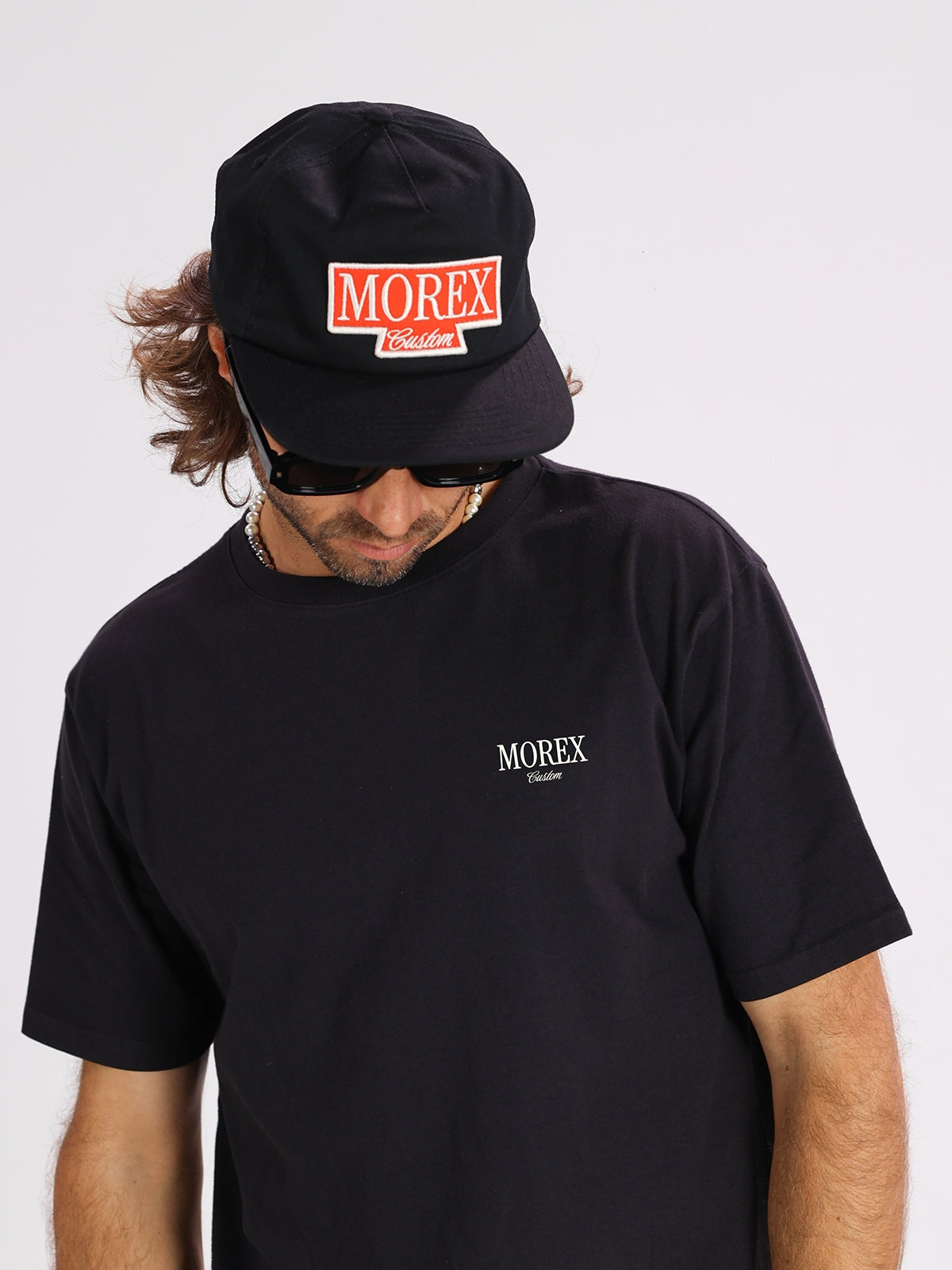 Homme portant un t-shirt noir Morex Custom et une casquette noire assortie avec logo rouge, style lifestyle et moto.
