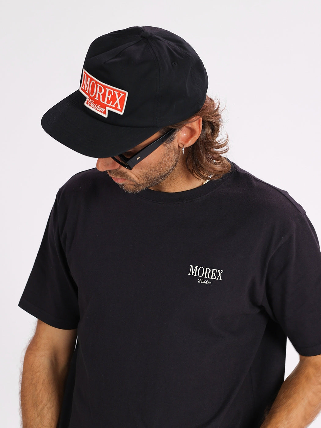 Homme portant un t-shirt noir Morex Custom avec logo blanc discret et une casquette noire assortie avec un patch logo rouge et blanc.