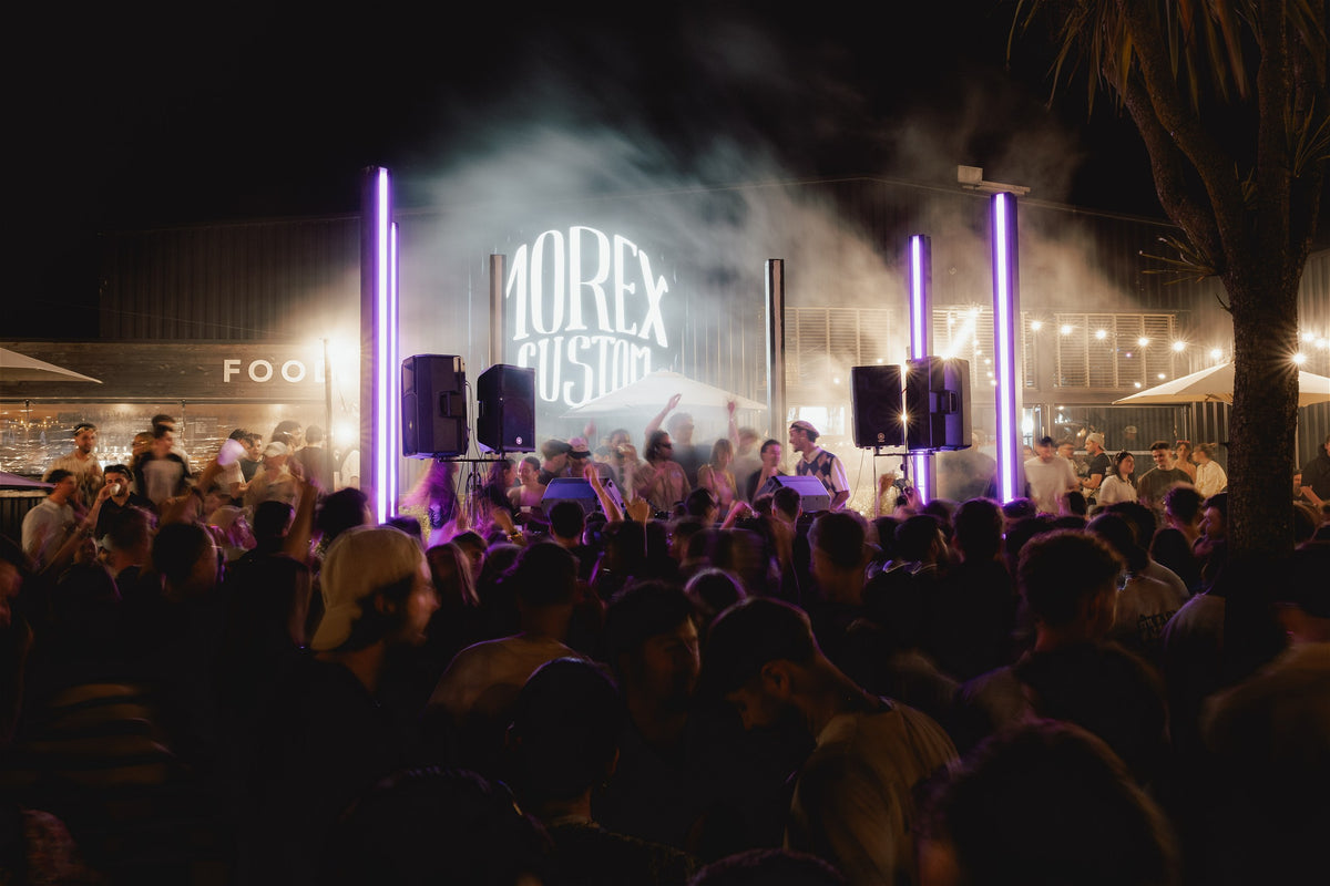 Ambiance électrique lors d'une soirée événementielle Morex Custom avec une foule dense, des néons violets et le logo de la marque illuminé dans une atmosphère festive et brumeuse.