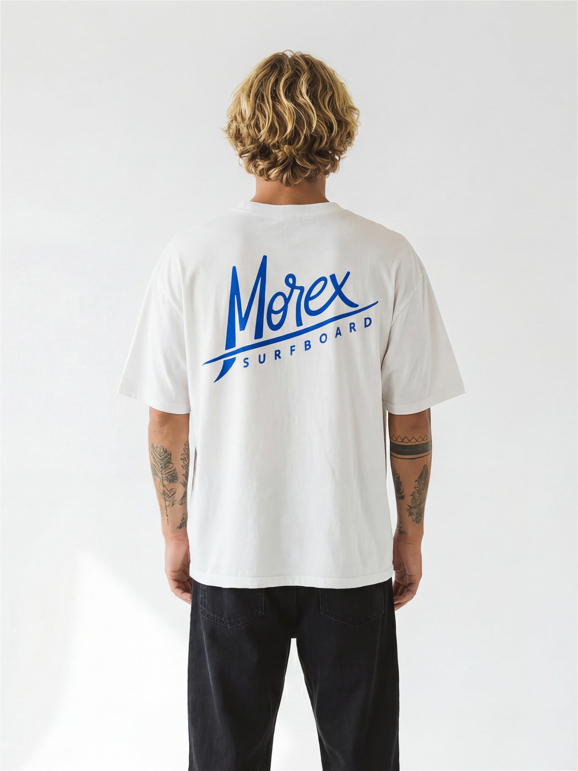 Vue arrière d'un homme portant un t-shirt blanc Morex Custom avec le logo bleu Morex Surfboard imprimé au dos.