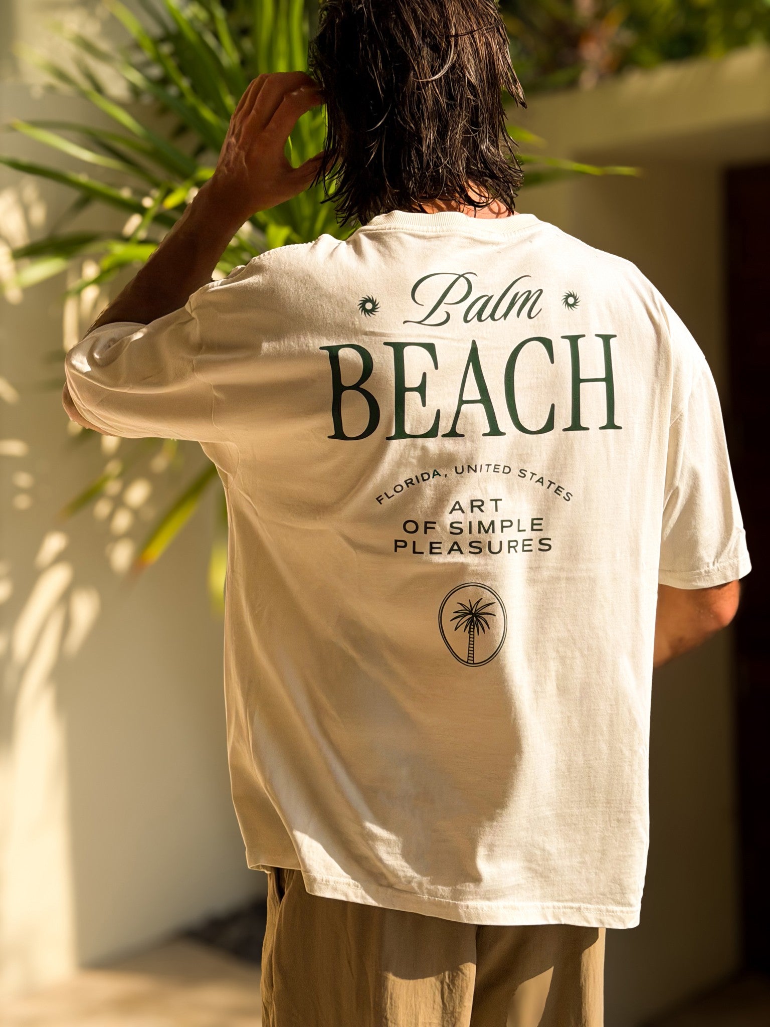 Homme de dos portant un t-shirt blanc Morex Custom avec inscription Palm Beach et logo palmier, style lifestyle décontracté.