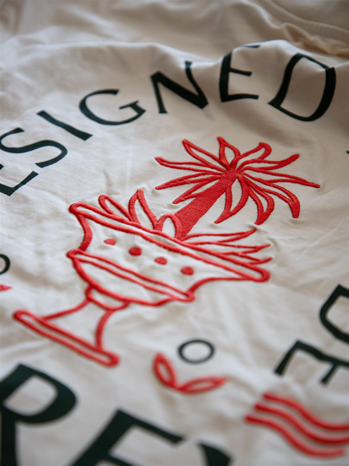 Gros plan sur la broderie rouge détaillée représentant un palmier vintage sur un t-shirt écru Morex Custom, esprit moto et lifestyle.