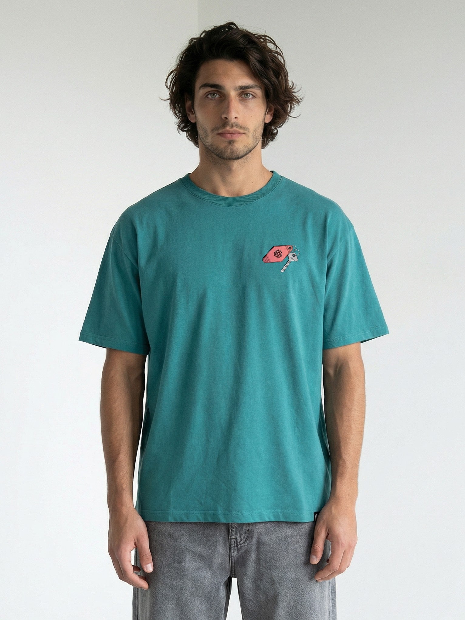 Homme portant un t-shirt Morex Custom de couleur teal avec un logo brodé sur la poitrine, idéal pour un look lifestyle décontracté.