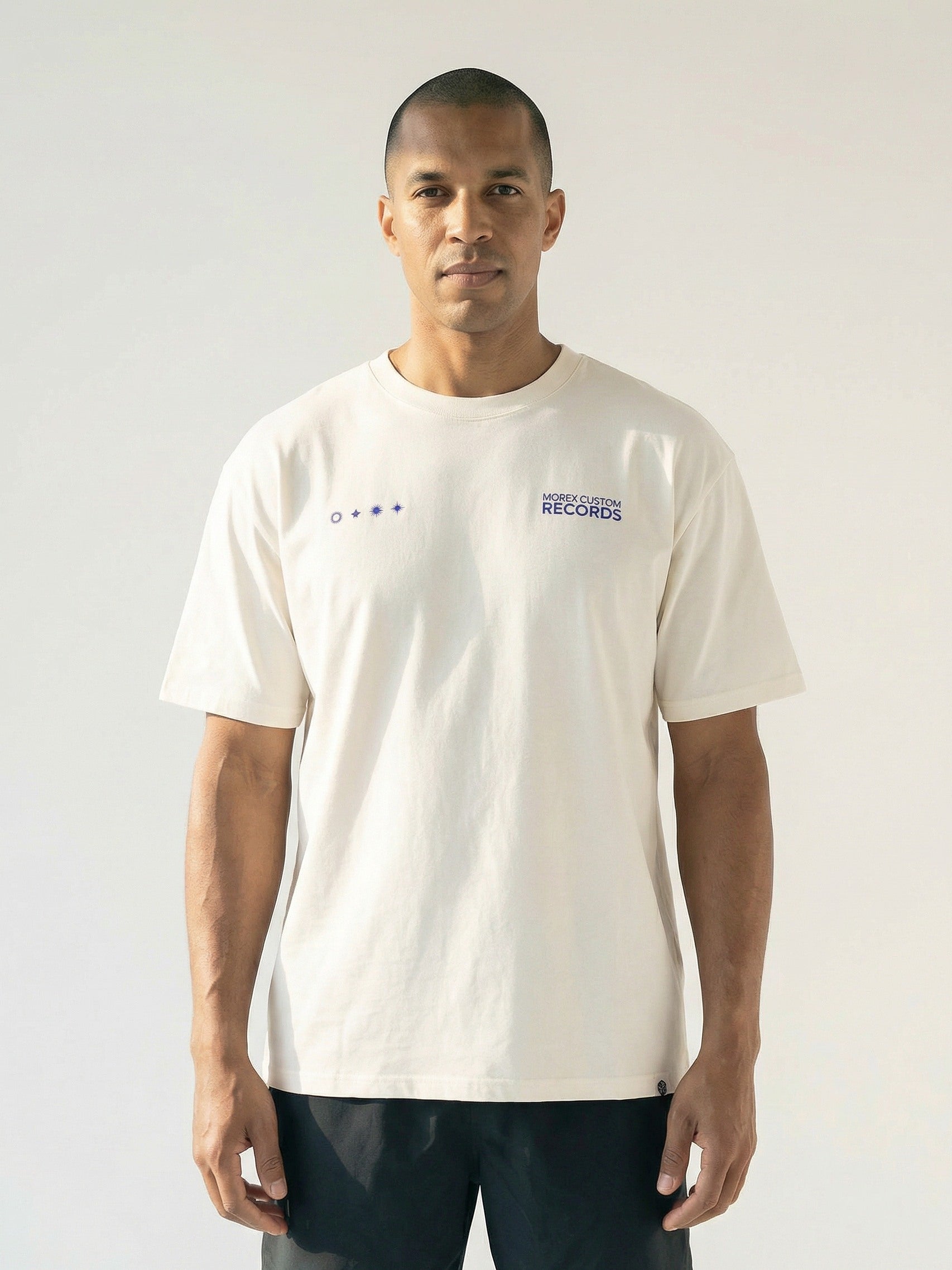 Homme portant un t-shirt crème Morex Custom avec logos graphiques bleus sur la poitrine, style lifestyle et moto.