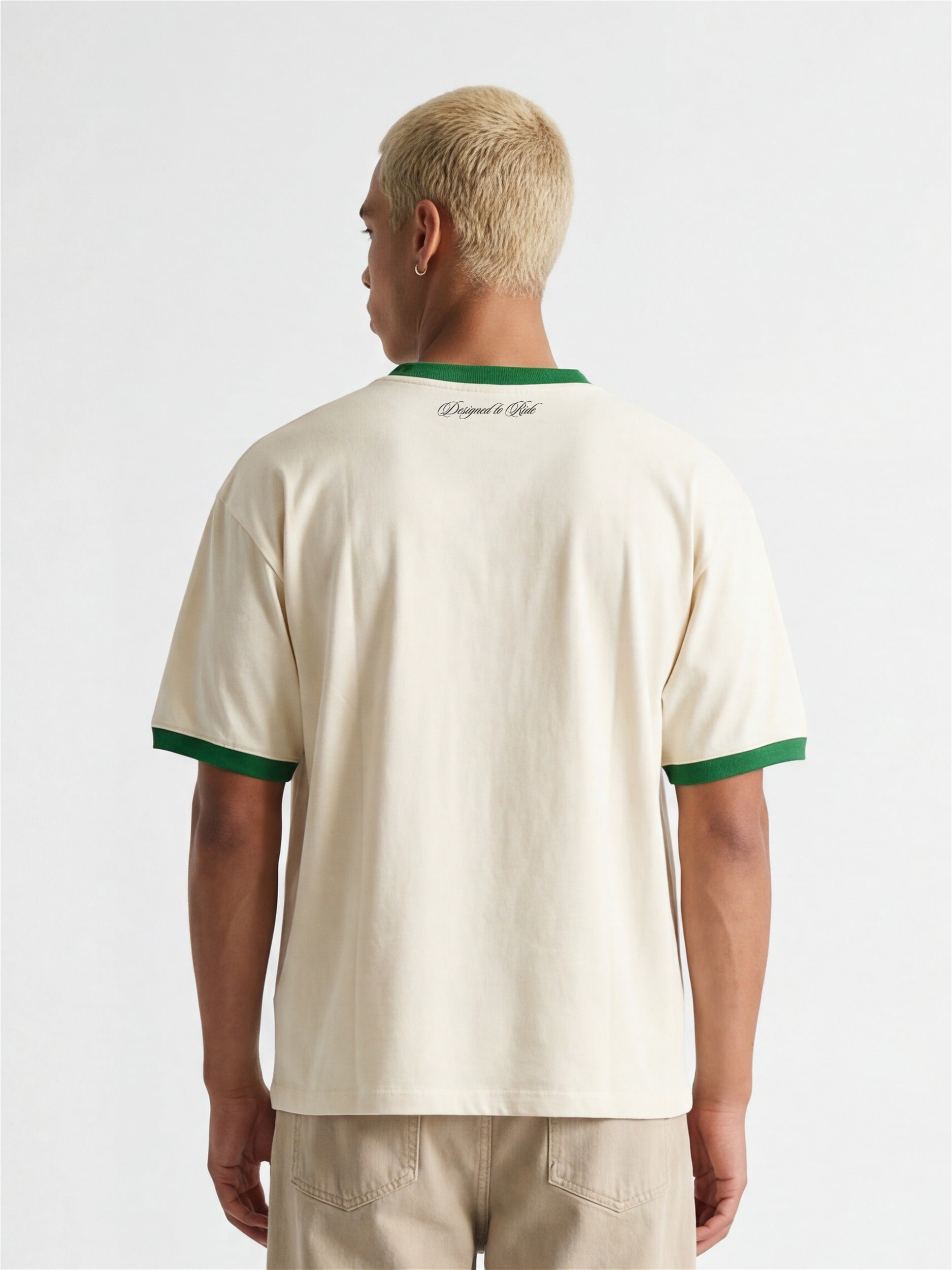 Vue de dos d'un homme portant un t-shirt ringer Morex Custom de couleur crème avec col et bordures de manches verts, associé à un pantalon beige.