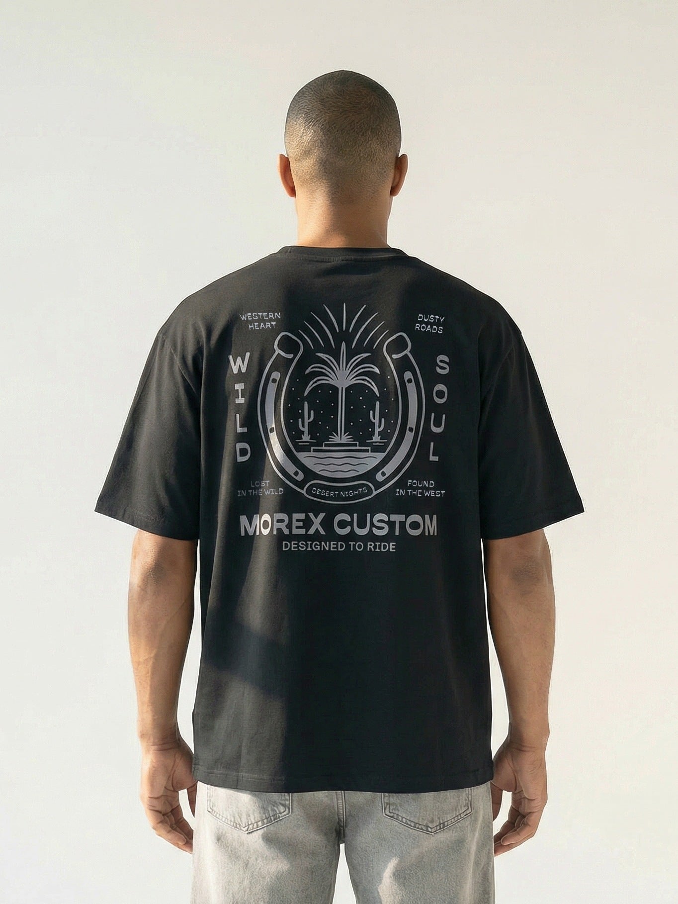 Vue de dos d'un homme portant un t-shirt noir Morex Custom avec un graphisme Wild Soul incluant un fer à cheval et un palmier.