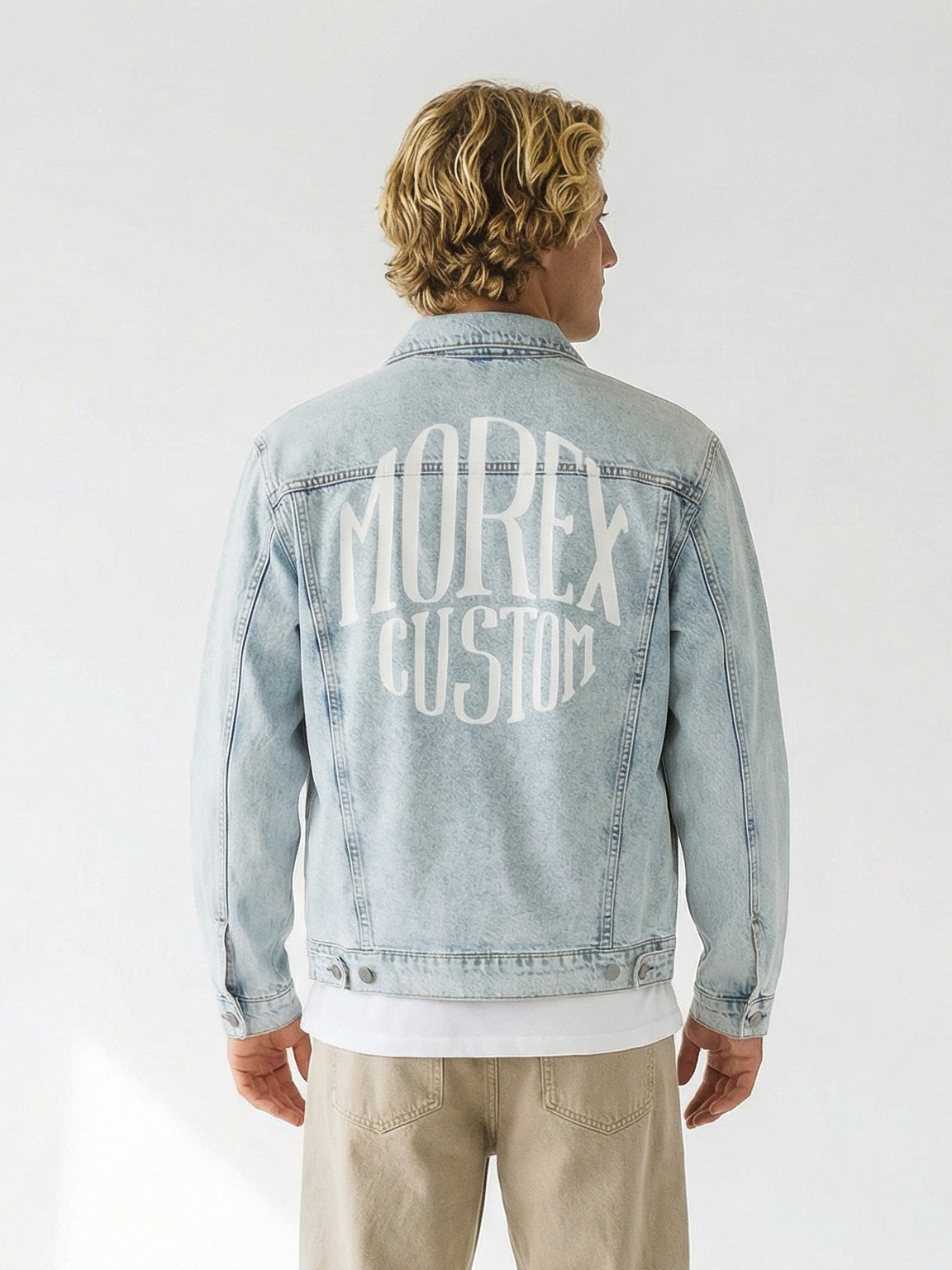 Homme de dos portant une veste en jean bleu clair délavée avec le logo Morex Custom blanc imprimé dans le dos, style lifestyle et moto.