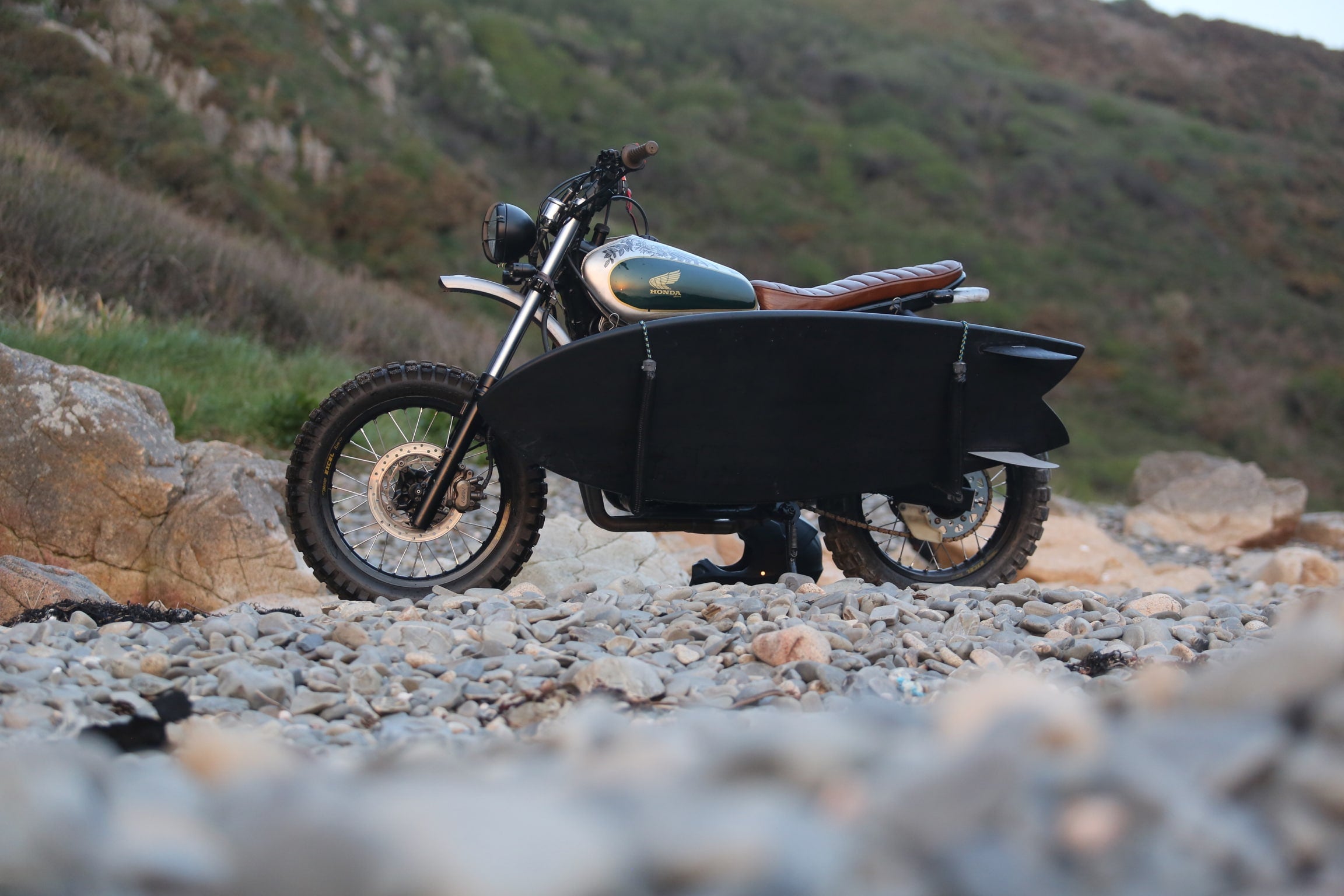 Honda custom dominator sur la plage avec un surf