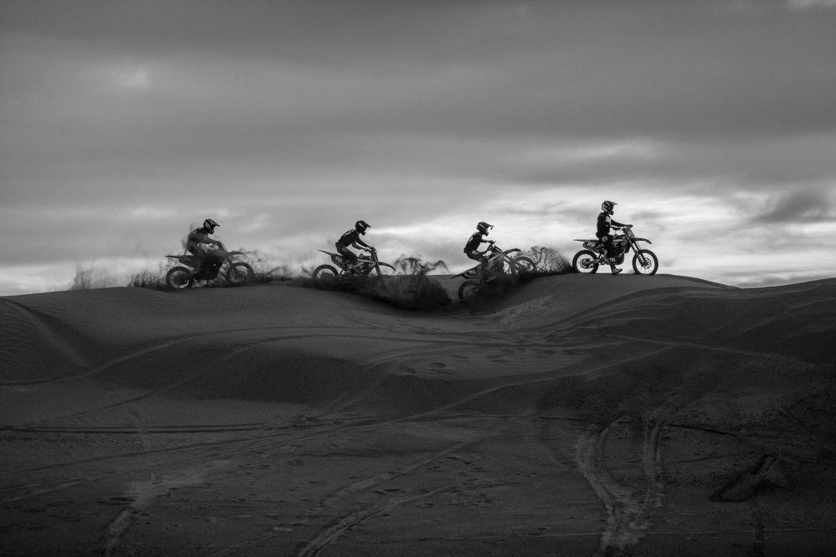 Quatre hommes sur des motos tout-terrain sur une dune de sable