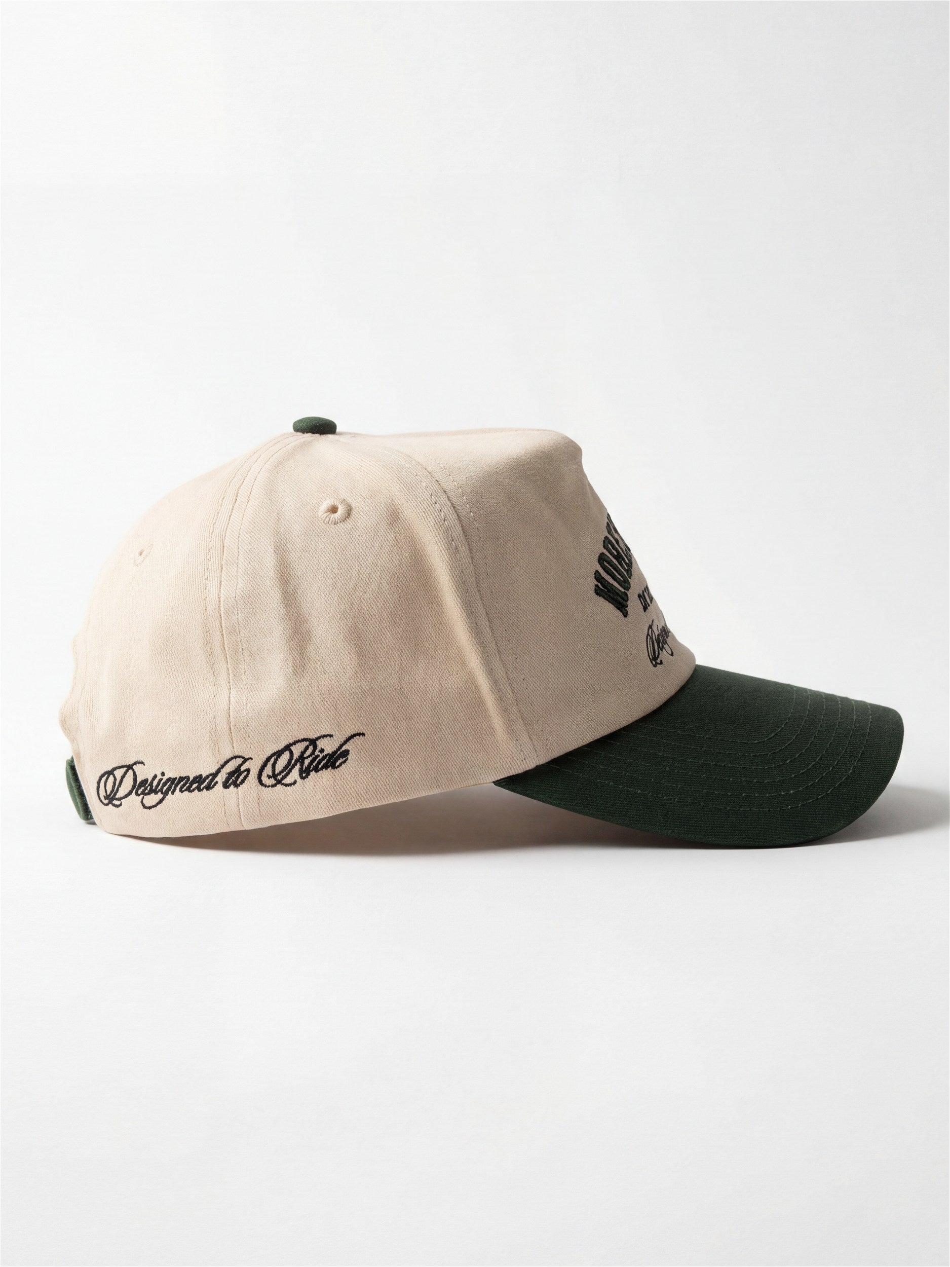 A side view of a Morex Custom two-tone baseball cap featuring a light beige textured crown and a dark green brim, with 'Designed to Ride' embroidered on the side.