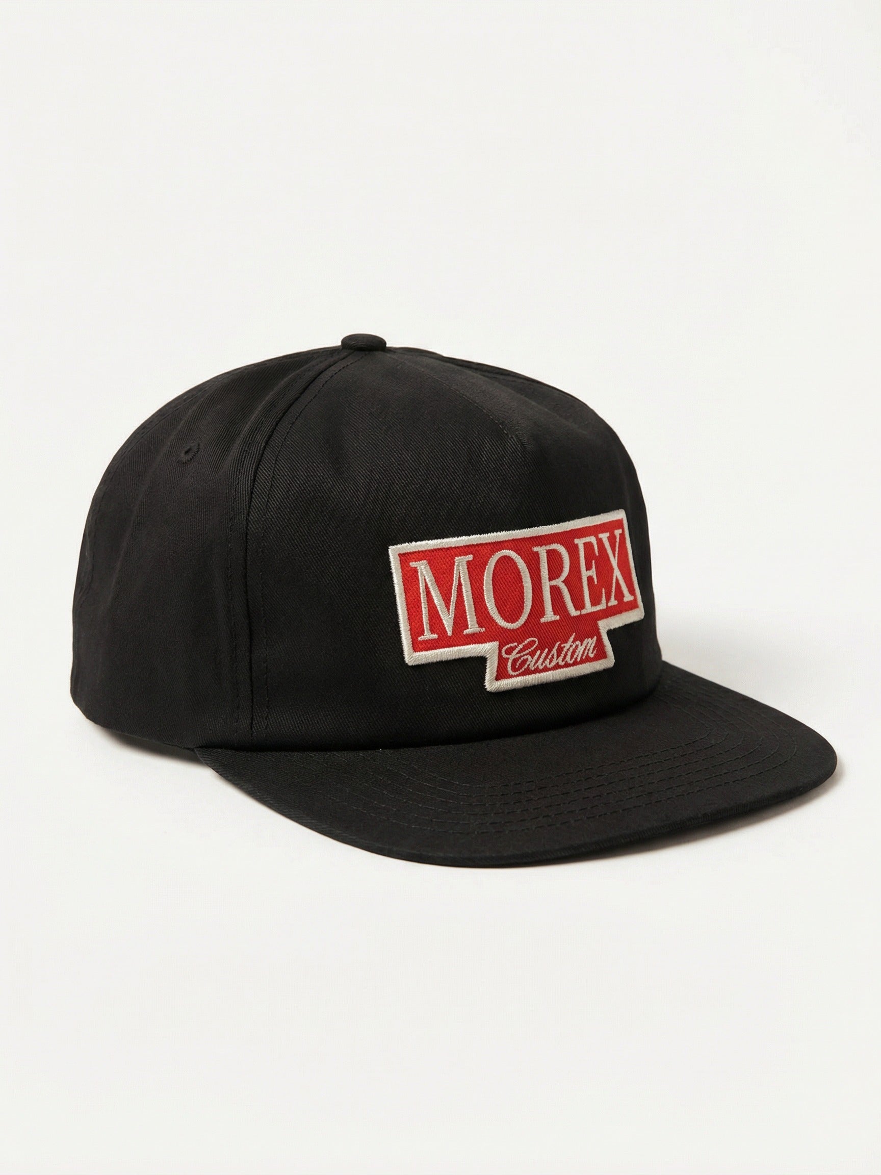 A black snapback baseball cap with a red rectangular patch on the front that says 'MOREX' in bold white letters and 'Custom' in script below it.