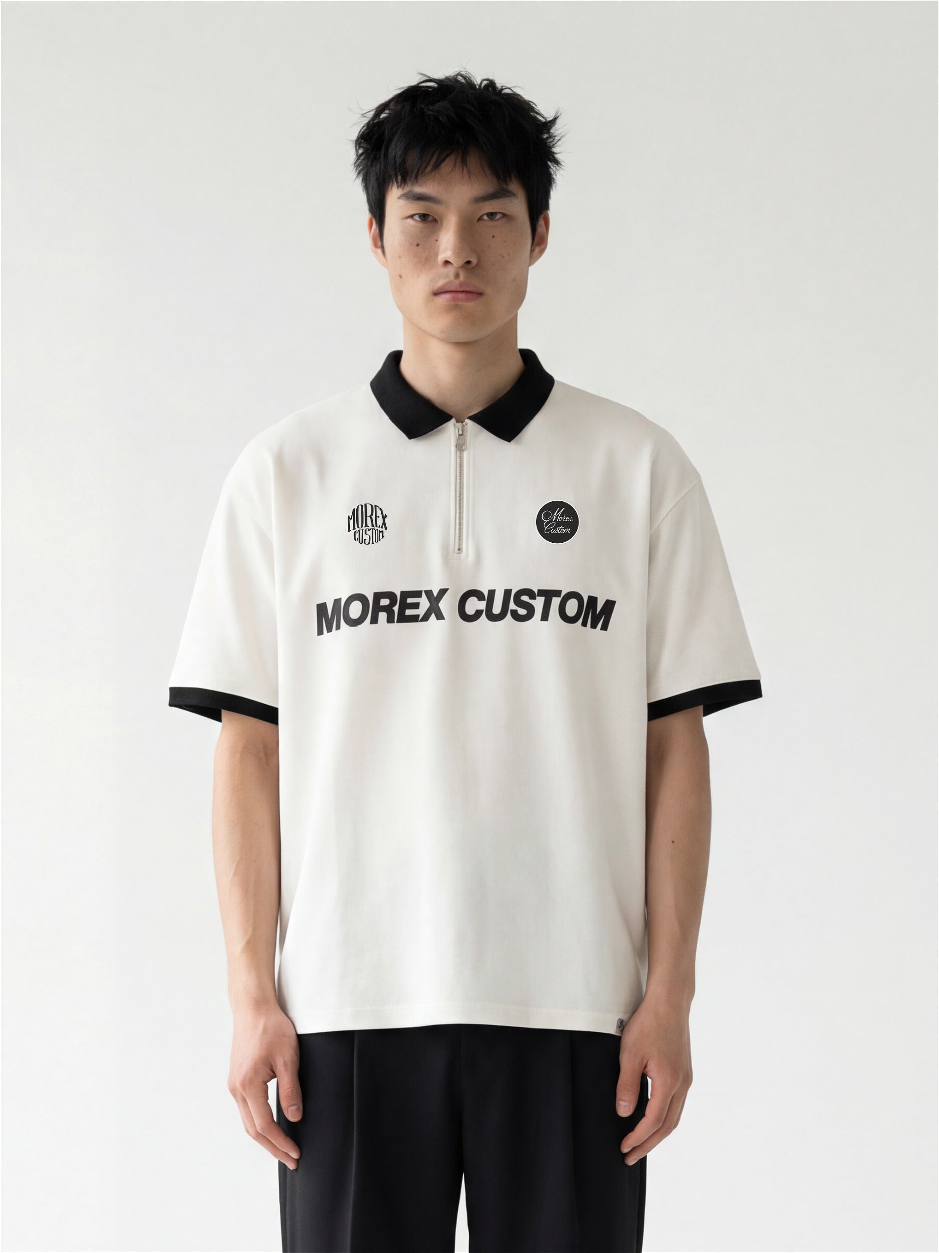Mannequin portant un polo blanc Morex Custom avec col zippé noir et inscription sur le torse, associé à un pantalon noir, style lifestyle et moto.