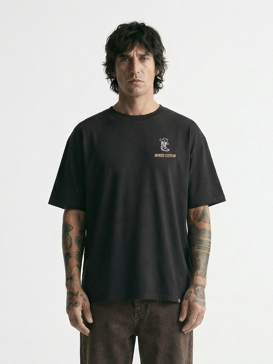 Homme portant un t-shirt noir à logo Morex Custom et un pantalon marron, look lifestyle et moto minimaliste sur fond blanc.