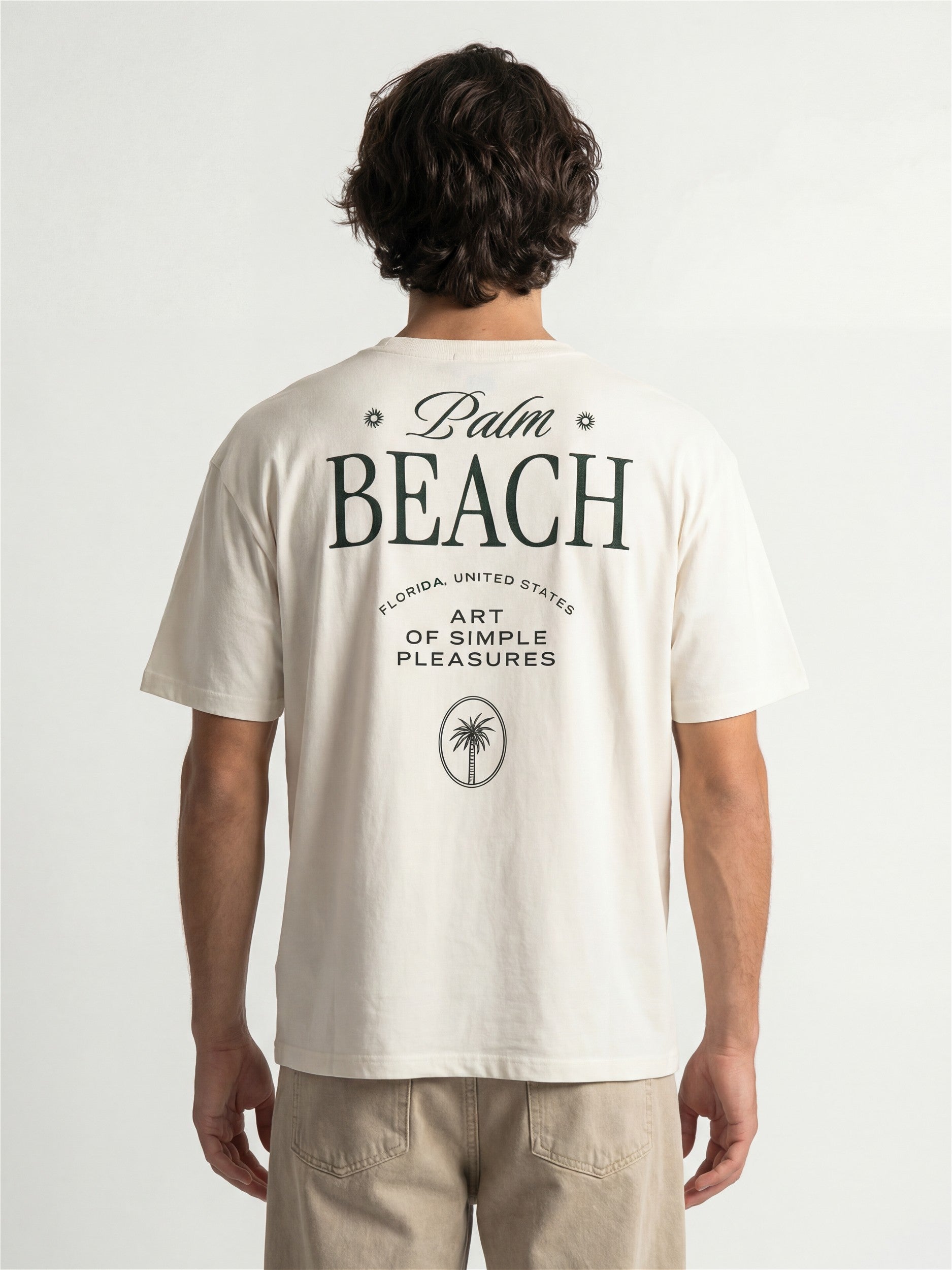 Dos d'un homme portant un t-shirt Morex Custom de couleur crème avec un imprimé graphique Palm Beach et Art of Simple Pleasures.