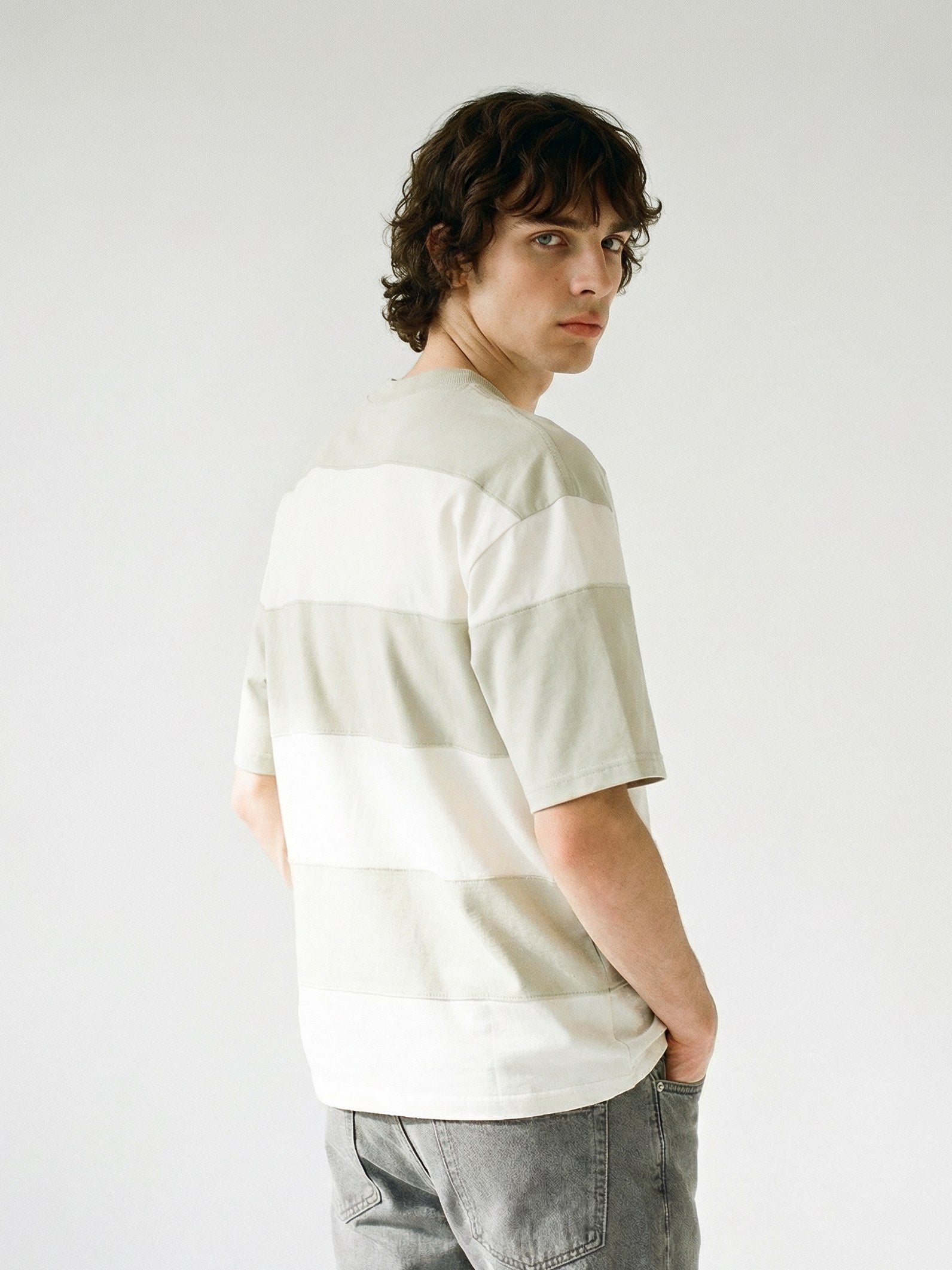 Un homme de dos portant un t-shirt à larges rayures horizontales grises et beiges de la collection Morex Custom lifestyle, regardant par-dessus son épaule.