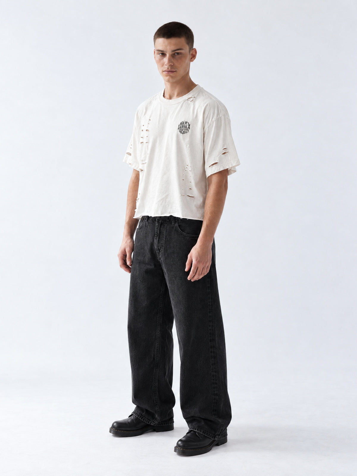 Modèle homme portant le t-shirt blanc cassé oversize effet vieilli et déchiré Morex Custom avec jean large noir délavé, look streetwear moto et lifestyle.