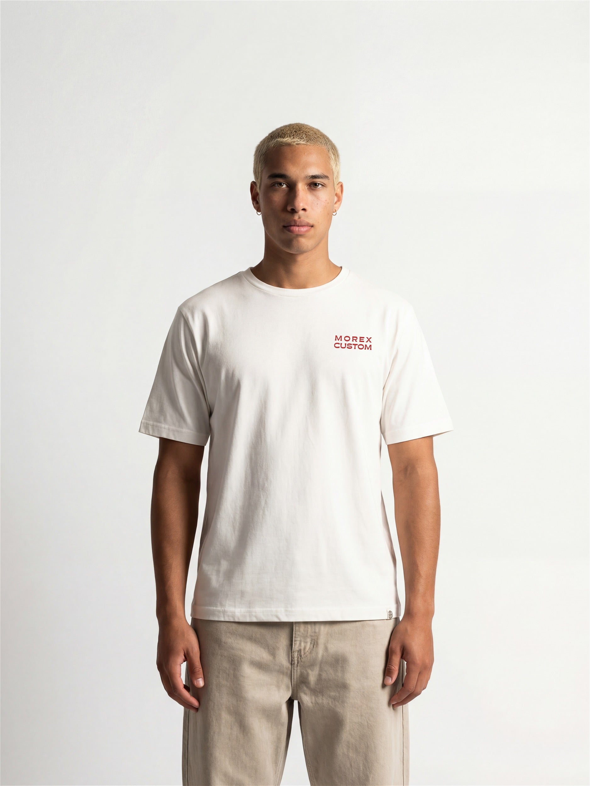 Homme portant un t-shirt blanc Morex Custom avec un petit logo rouge sur la poitrine et un pantalon beige, style moto lifestyle.