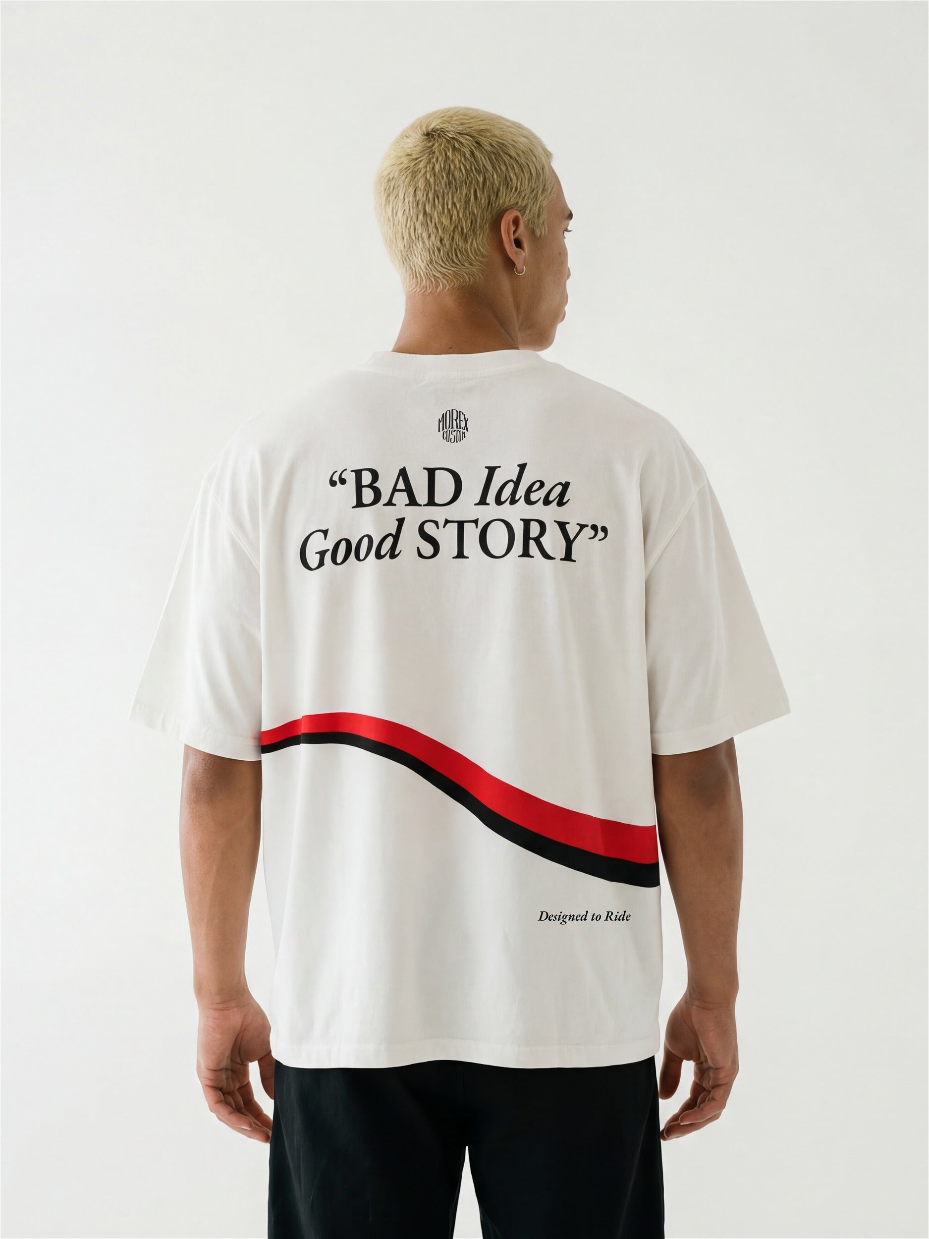 Vue de dos d'un homme portant un t-shirt blanc oversize Morex Custom avec le slogan 'BAD Idea Good STORY' et un graphisme de vague rouge et noir.