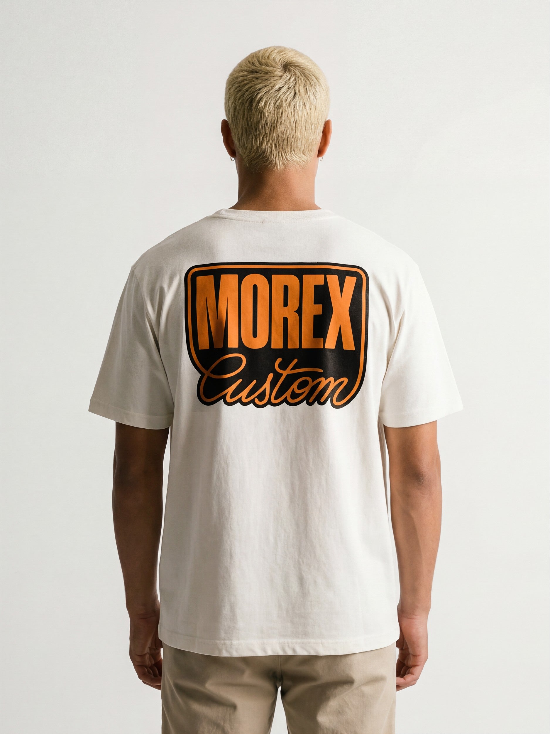 Homme de dos portant un t-shirt blanc Morex Custom avec un grand logo graphique orange et noir sur le dos, style lifestyle et moto.