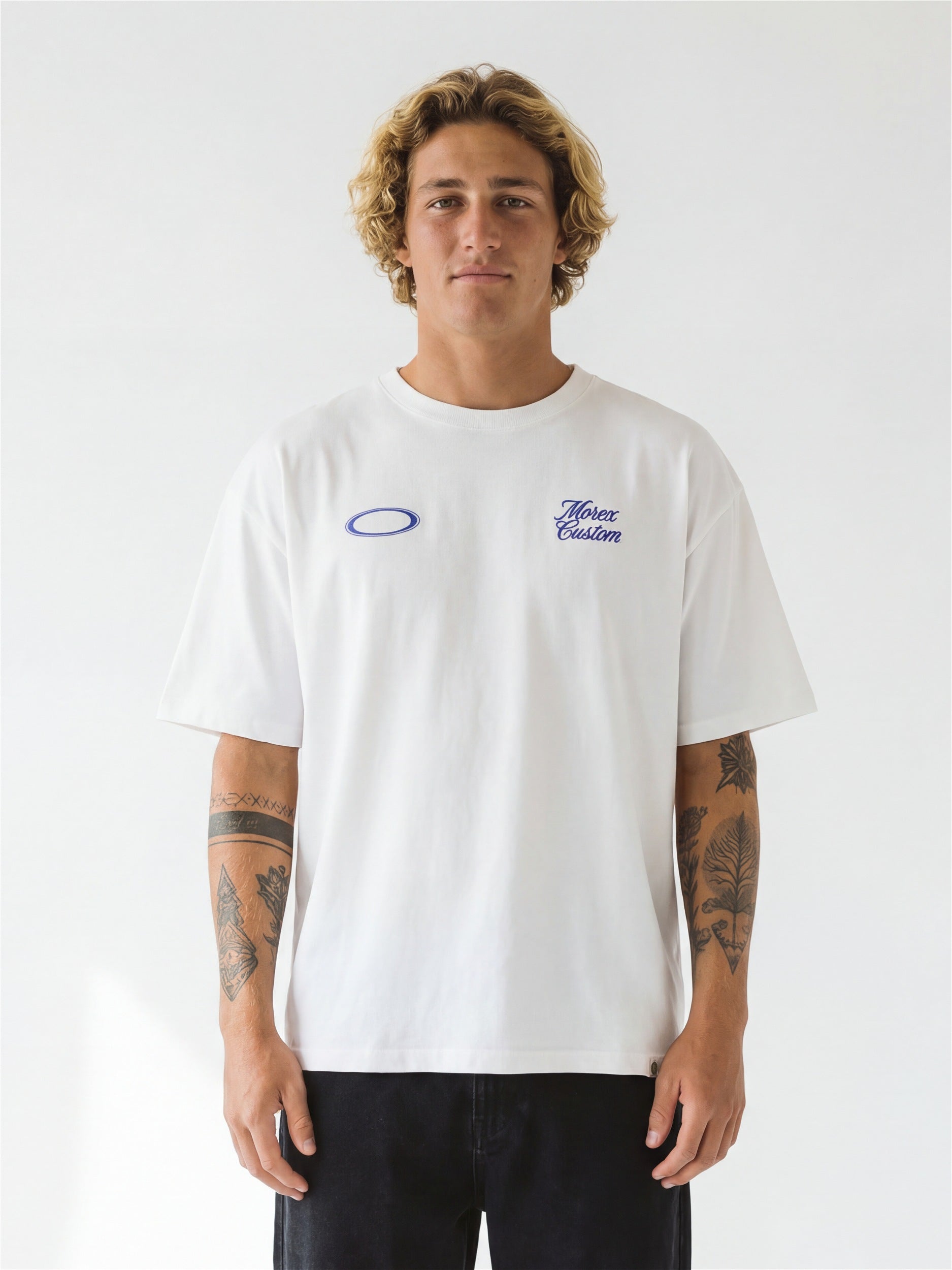 Homme portant un t-shirt blanc de la marque Morex Custom avec deux logos bleus discrets sur la poitrine, style décontracté moto et lifestyle.