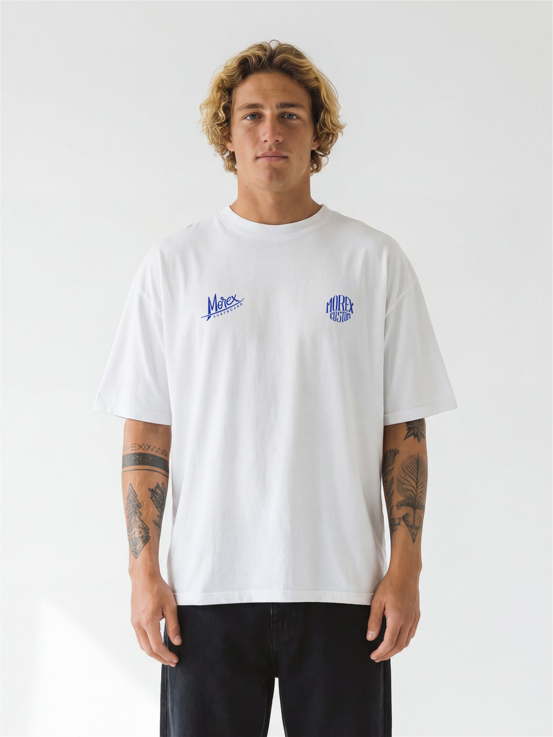 Homme portant un t-shirt blanc Morex Custom avec logos bleus sur la poitrine, coupe décontractée, style lifestyle surf et moto.