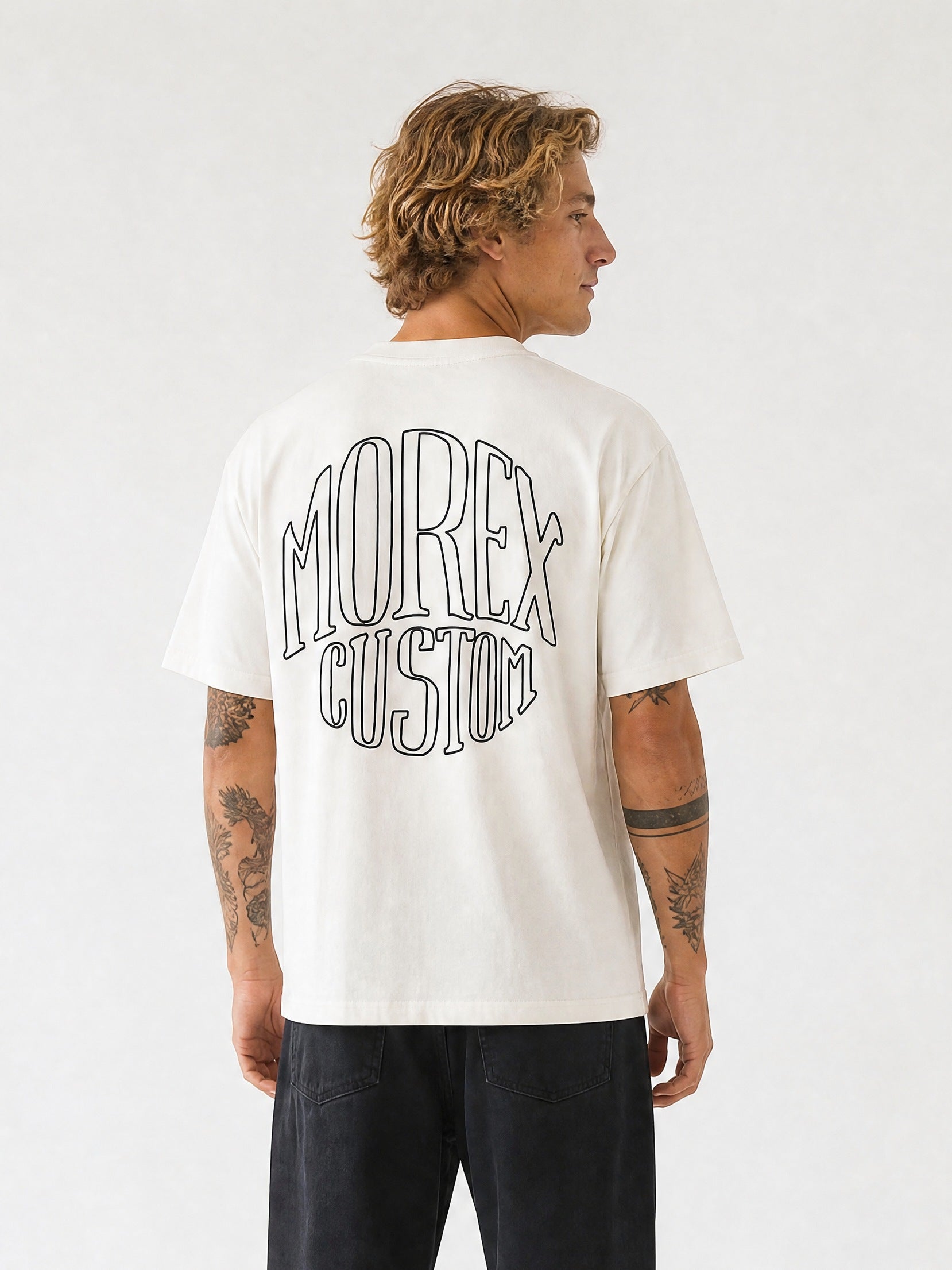 Homme vue de dos portant un t-shirt blanc crème avec un grand logo graphique noir Morex Custom imprimé au dos et un pantalon noir.