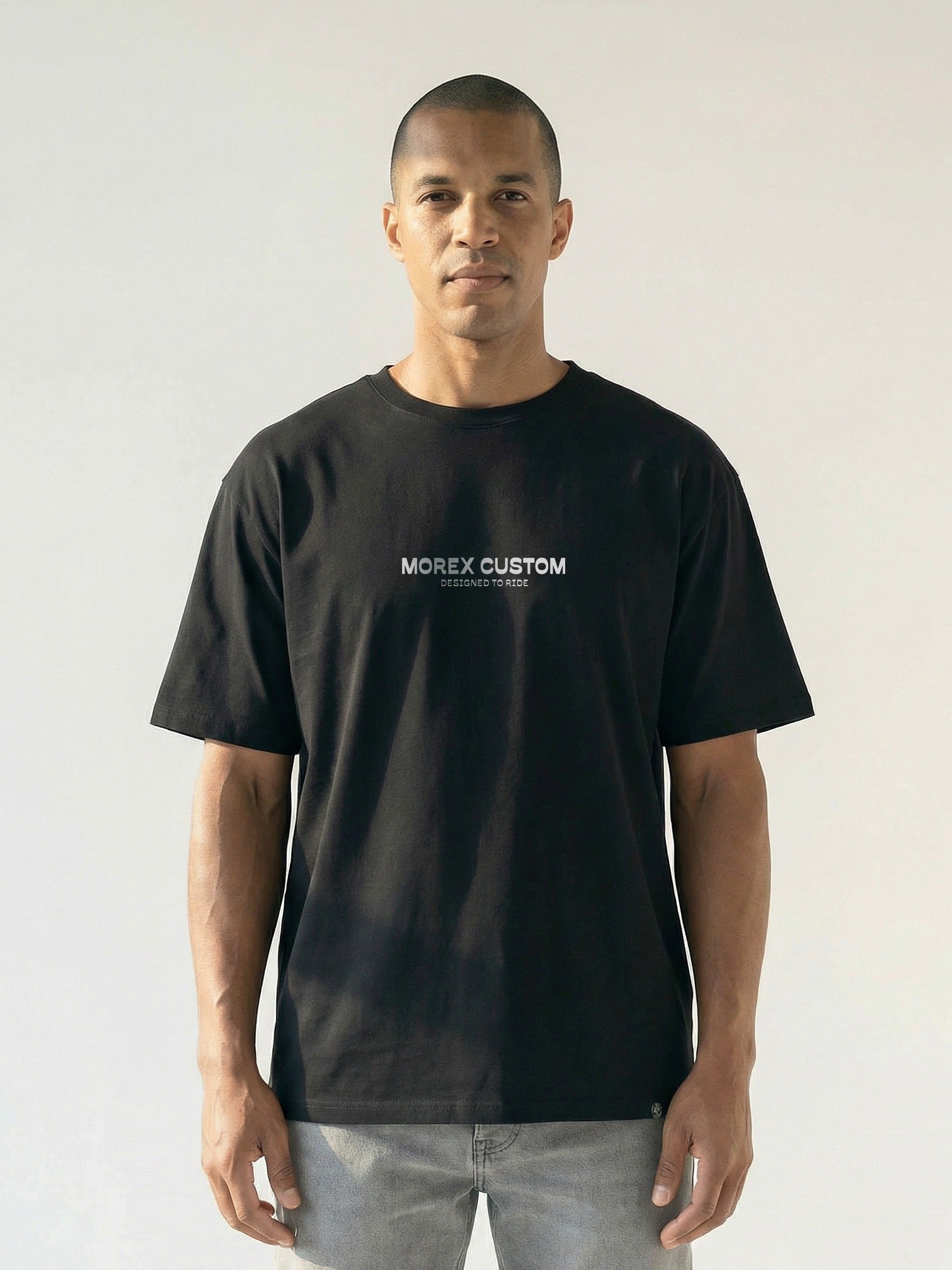 Un homme portant un t-shirt noir Morex Custom avec le logo blanc imprimé sur le torse, style lifestyle moto.