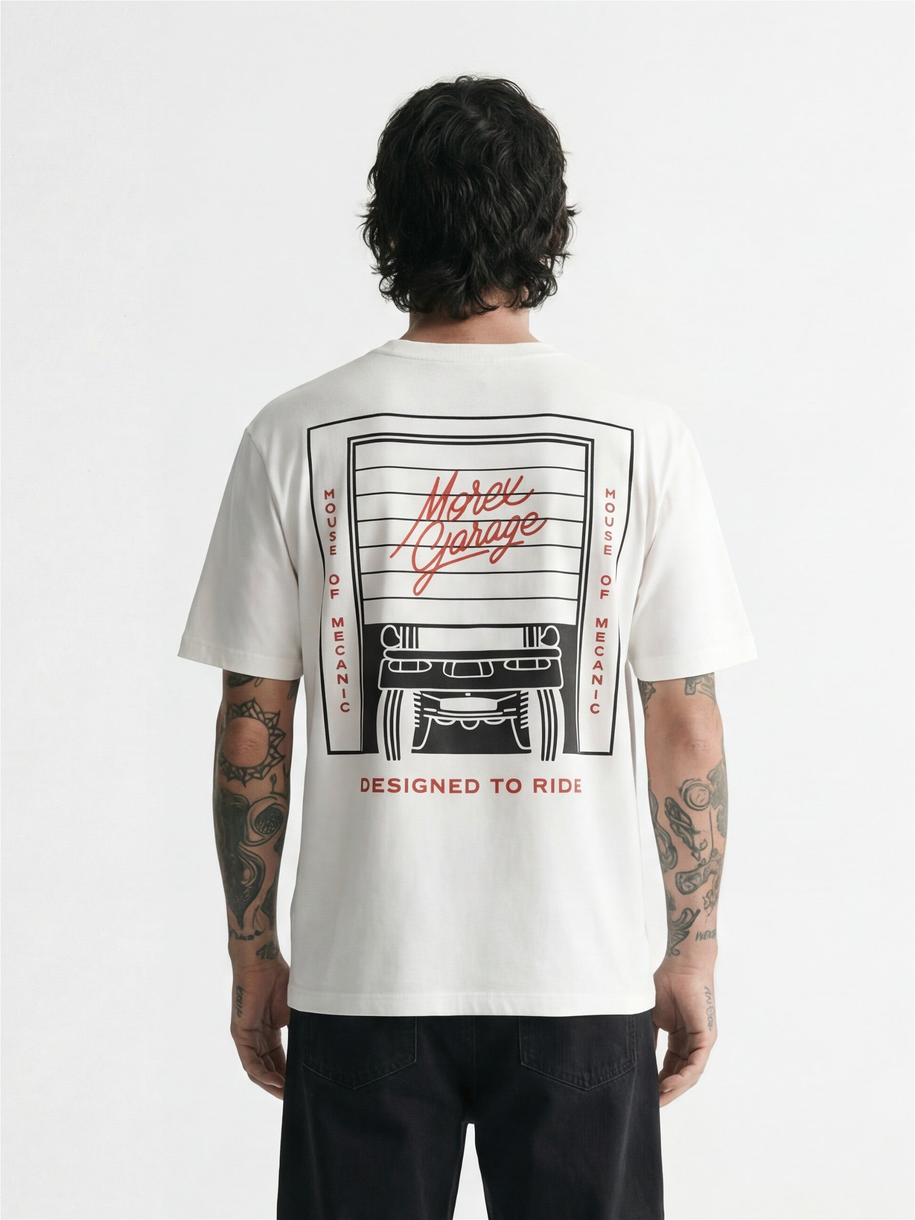Vue de dos d'un homme portant un t-shirt blanc de la marque Morex Custom avec un graphisme noir et rouge représentant un garage et l'inscription 'Designed to Ride'.