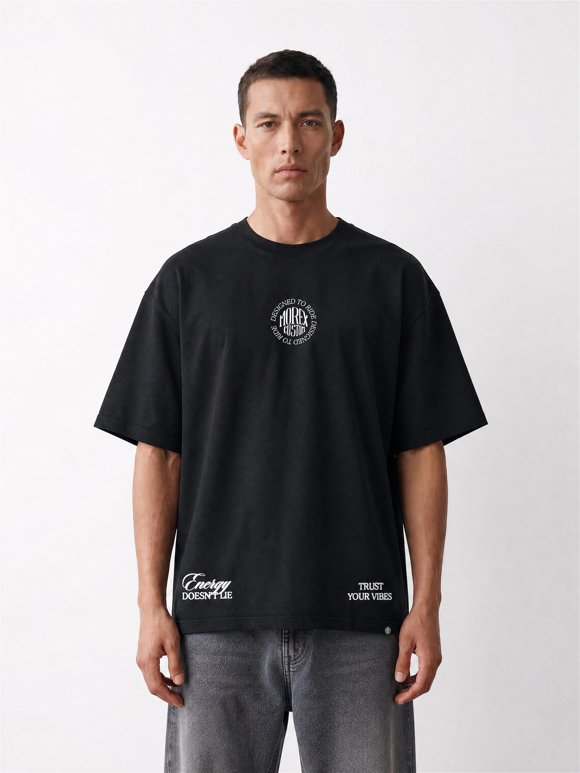 Homme portant un t-shirt noir Morex Custom à coupe oversized avec des graphismes blancs sur la poitrine et le bas, style moto et streetwear.